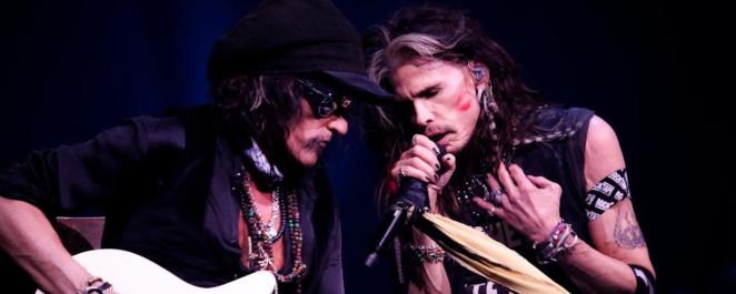 Two members of Aerosmith lean into each other as they perform songs like "Dude (Looks Like A Lady)."