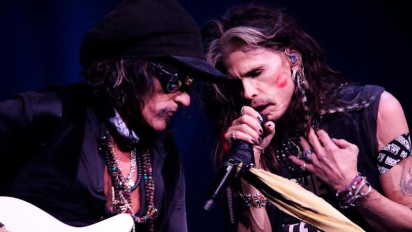 Two members of Aerosmith lean into each other as they perform songs like "Dude (Looks Like A Lady)."