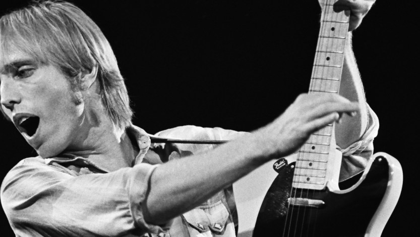 Tom Petty performing live with his guitar held high.