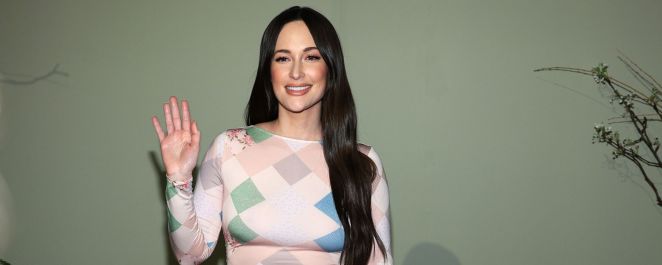 Kacey Musgraves waves in a pink multi-patterned dress.