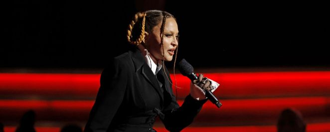 Madonna, dressed in a black suit, speaks into a microphone at the 2023 GRAMMY Awards.