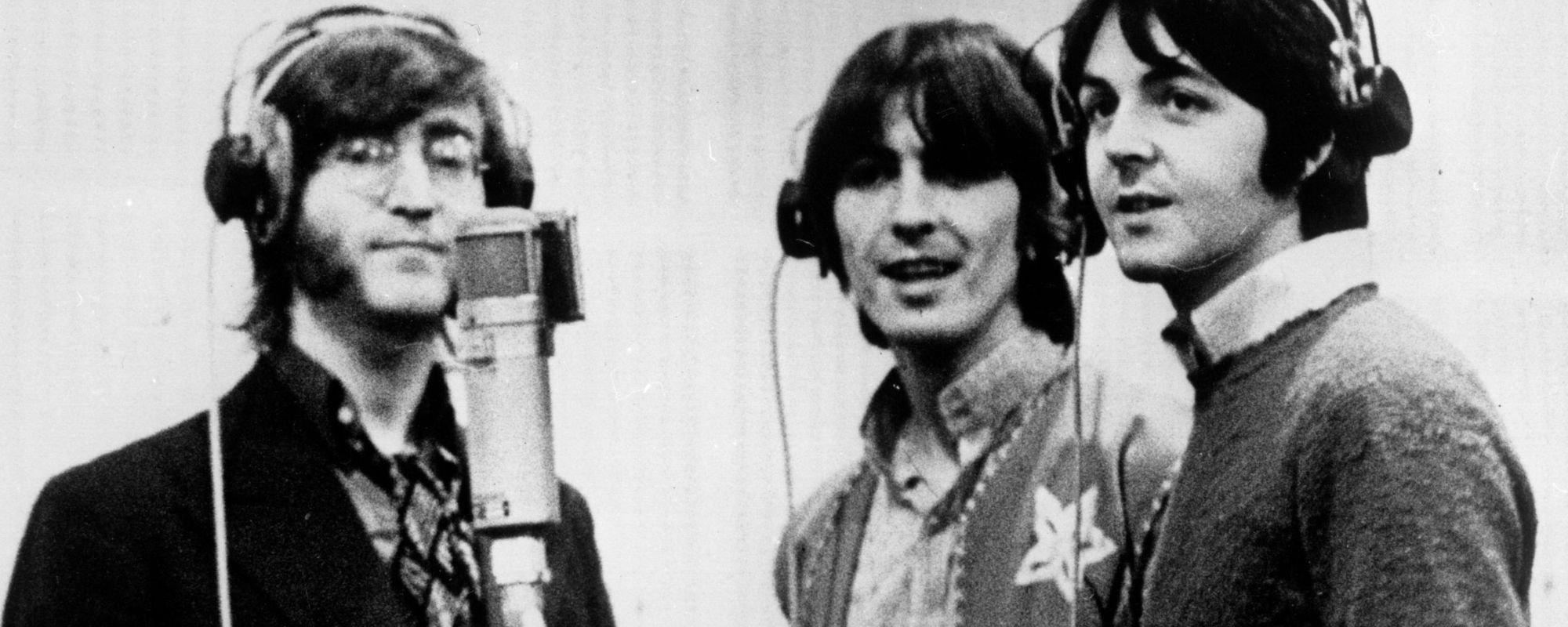 John Lennon, George Harrison, and Paul McCartney stand around microphone