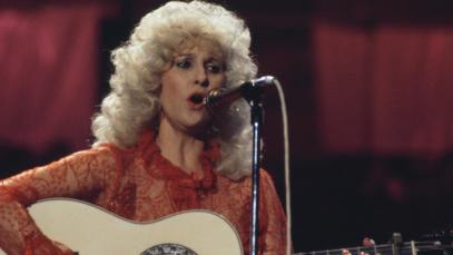 Tammy Wynette (1942-1998), U.S. country music singer-songwriter, singing into a microphone and playing the guitar during a live concert performance at the Country Music Festival, at Wembley Arena, London, England, Great Britain, in April 1981.