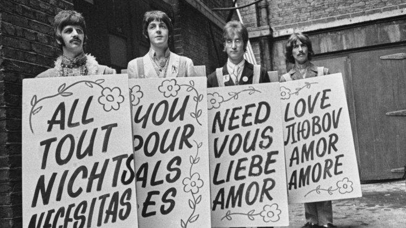 The Beatles posing with sandwich signs that say "All you need is love" in different languages
