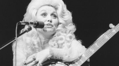 Dolly Parton speaking into mic, holding banjo