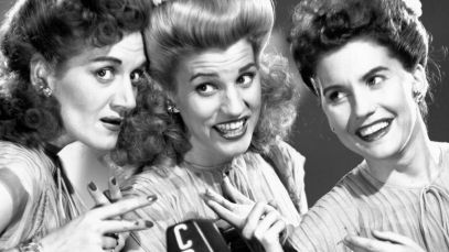 Andrews Sisters, group who sang location-specific Christmas song "Mele Kelikimaka," posing around mic