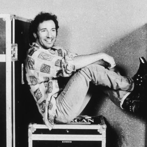 28th July 1992: American musician Bruce Springsteen sits on a trunk with his feet up backstage at the Brendan Byrne Arena in the Meadowlands sports complex, East Rutherford, New Jersey. Springsteen wears a casual shirt with faded jeans and a pair of cowboy boots with chains and metal tips. (Photo by Keith Meyers/New York Times Co./Getty Images)